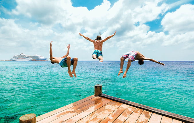 Three boys diving off of a wooden platform into the ocean