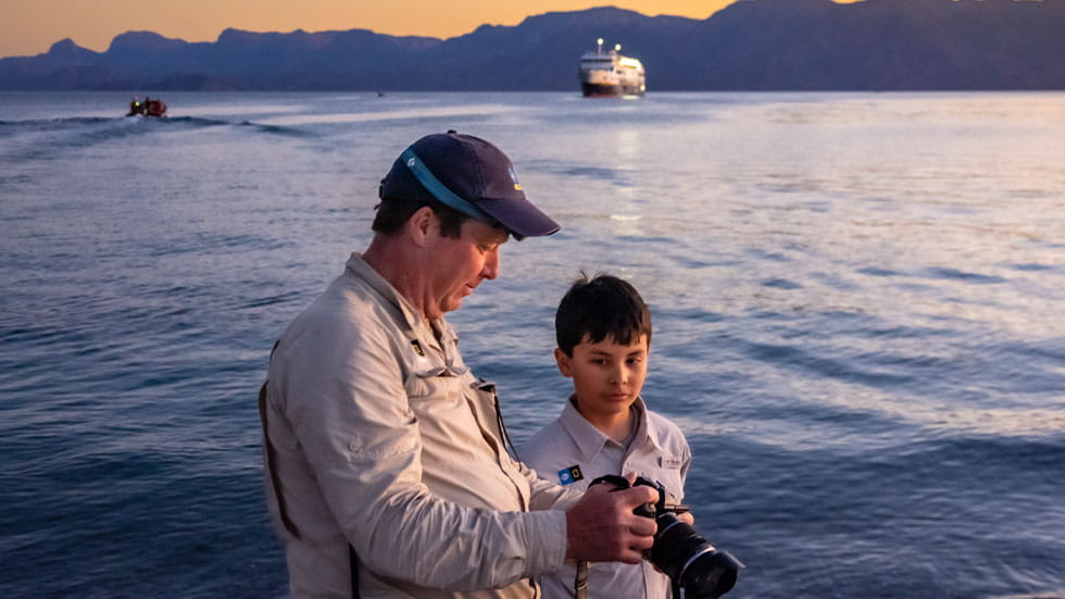 mand and boy looking at camera, water and ships in background