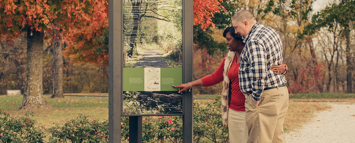 Visitors looking at a wayside placard before stolling the Carver Trail. Photo Credit Mark Neuenschwander