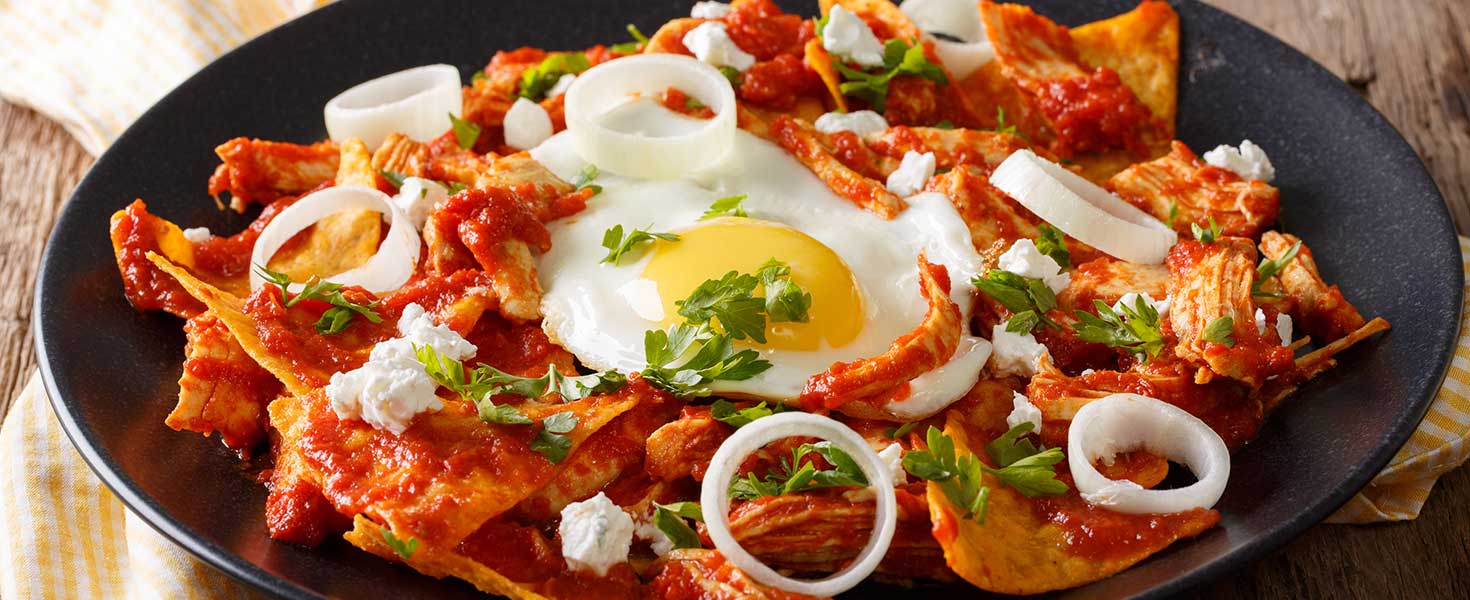 Mexican nachos with tomato salsa, chicken and egg close-up on a plate.