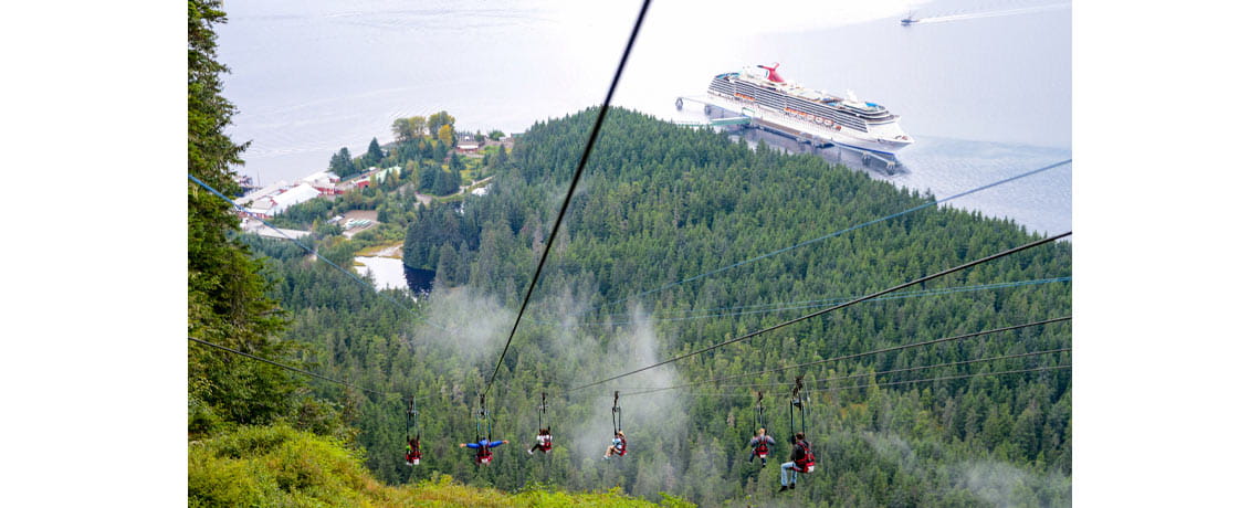 Cruise line passengers ride a zipline while the cruise ship, Carnival Miracle is in the background 