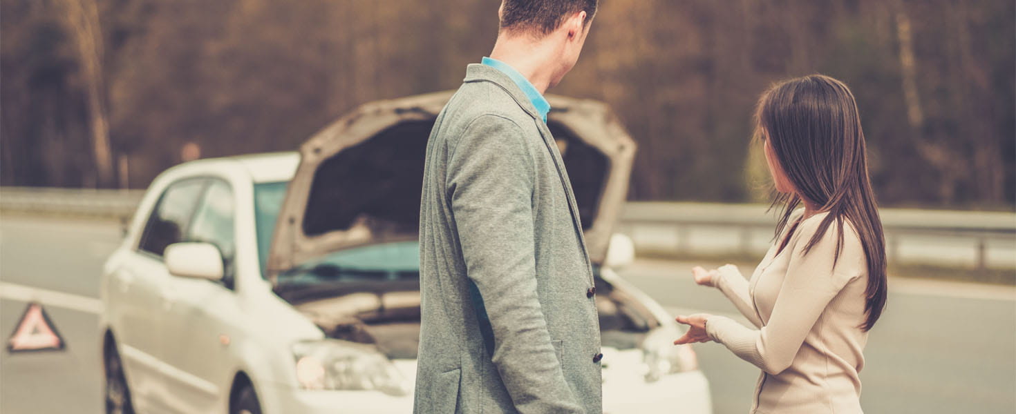 Man and Woman standing in front of broken down car on side of road