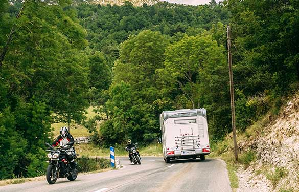 Motorcycle and motorhome driving in different directions on a mountain top road.