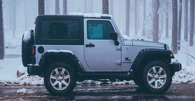 Grey jeep parked on the side of the road during a snow storm.