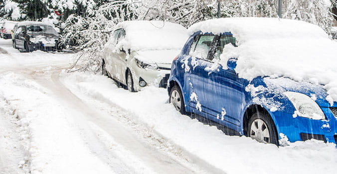 Blue and White snowed covered cars stuck on the side of the road.