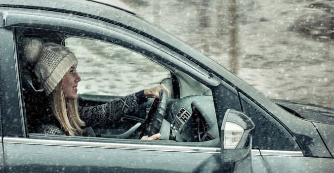 Young female driving down the road with snow falling down.