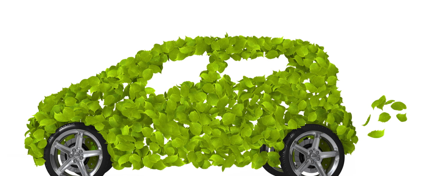 A green car is made up entirely of green leaves set on four tires with fancy chrome wheels.