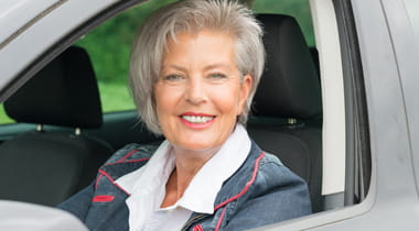 Older woman sitting in driver's seat of car smiling