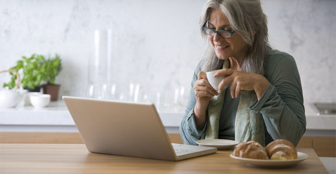 Older woman holding coffee mug reading something on a laptop