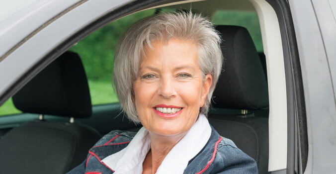 Older woman sitting in driver's seat of car smiling