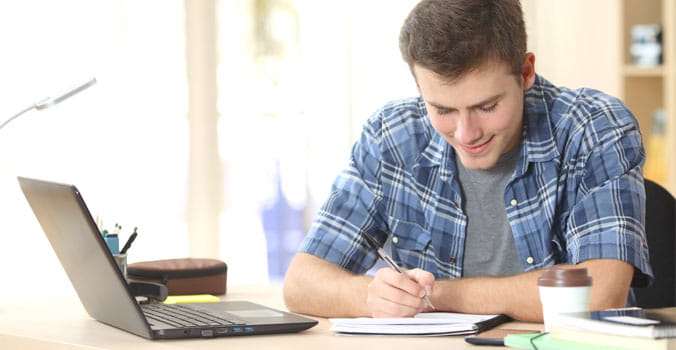 Young man writing in front of a laptop