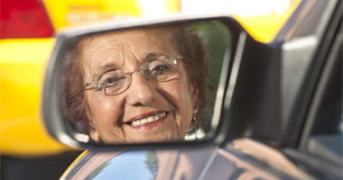 Senior Citizen Smiling with her face in the side mirror