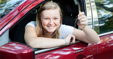 Blond teenage girl sitting in her new car, holding the keys