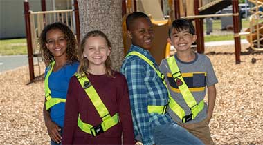 Group of smiling safety patrol kids standing around a tree.