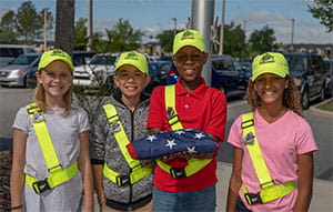 Group of school safety patrol kids in uniform holding a folded american flag.