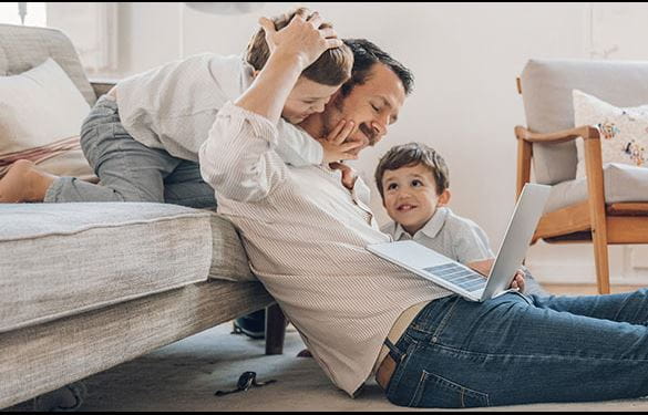 Father sitting on floor with laptop playing with his two young children