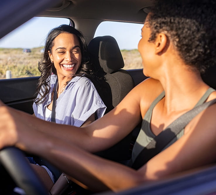 Beautiful latin hispanic woman with best friend enjoying and laughing in car while going on a road trip.