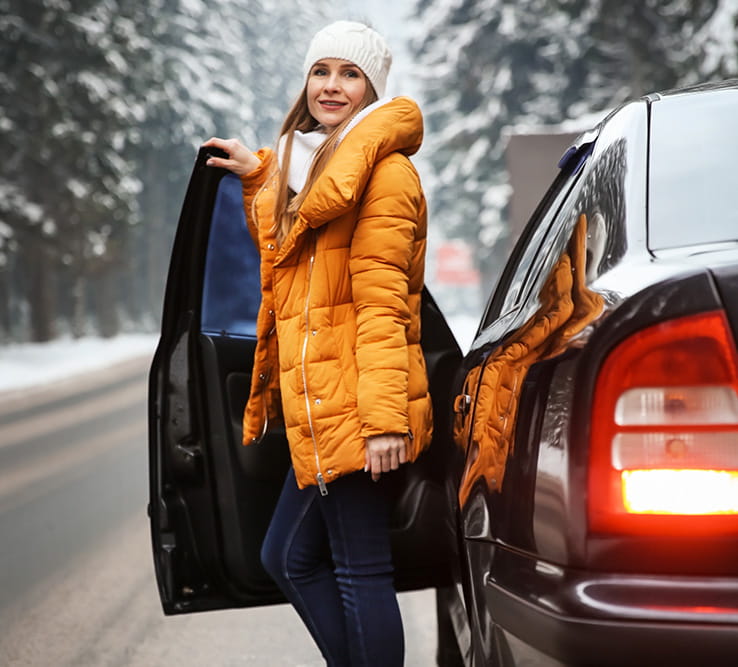 Woman standing next to an open car door on a snowy road.