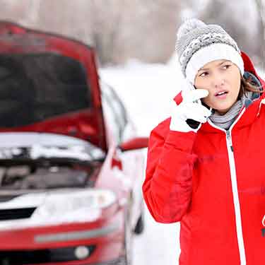woman on phone in coat hat and mittens in front of car with open hood