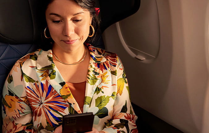 Woman looks at her cellphone as she sits in a window seat of a plane