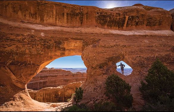 Arches National Park  - view of partition arch - a tourist stands inside opening