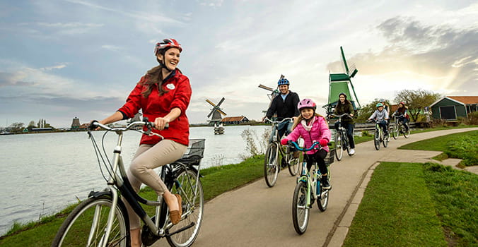 In The Netherlands, a happy family rides bikes past colorful windmills and the placid waters of a canal.