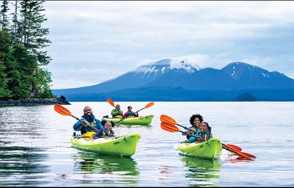 Families kayaking in Alaska waters with snow-capped mountains in distance