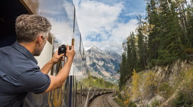 Man taking photo of Canadian Mountains from train observation deck