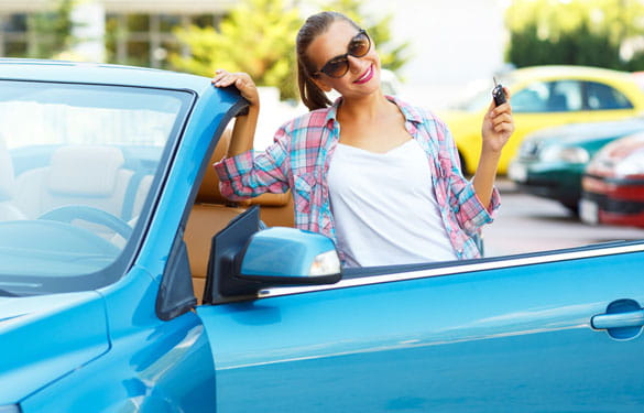 Young lady standing outside of car holding keys on sunny day