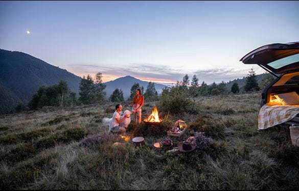 Two people having a picnic with campfire overlooking the mountains and sunset, with their dog.