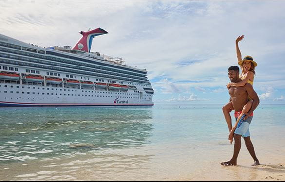 Couple walking on beach towards the water, with Carnival cruise ship off the beach.