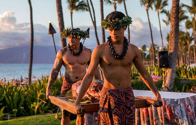 Wailea beach, Maui: Roast pig getting ready by traditionally dressed Hawaiian men during luau on beach in Maui.