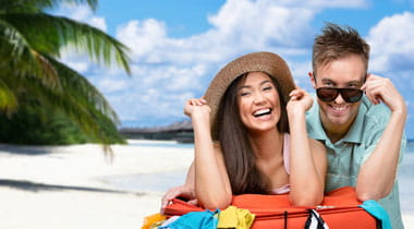 Happy couple leaning on luggage with beach in background