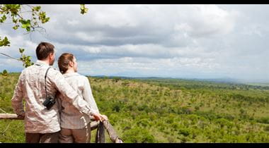 Couple on safari vacation looking to savanna from balcony