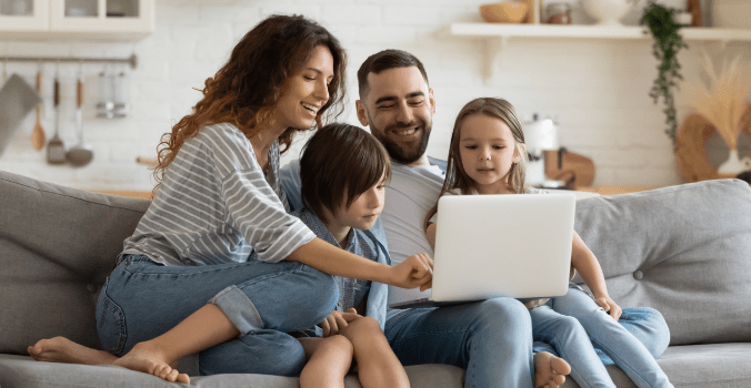 Family of four together looking at a laptop on the couch
