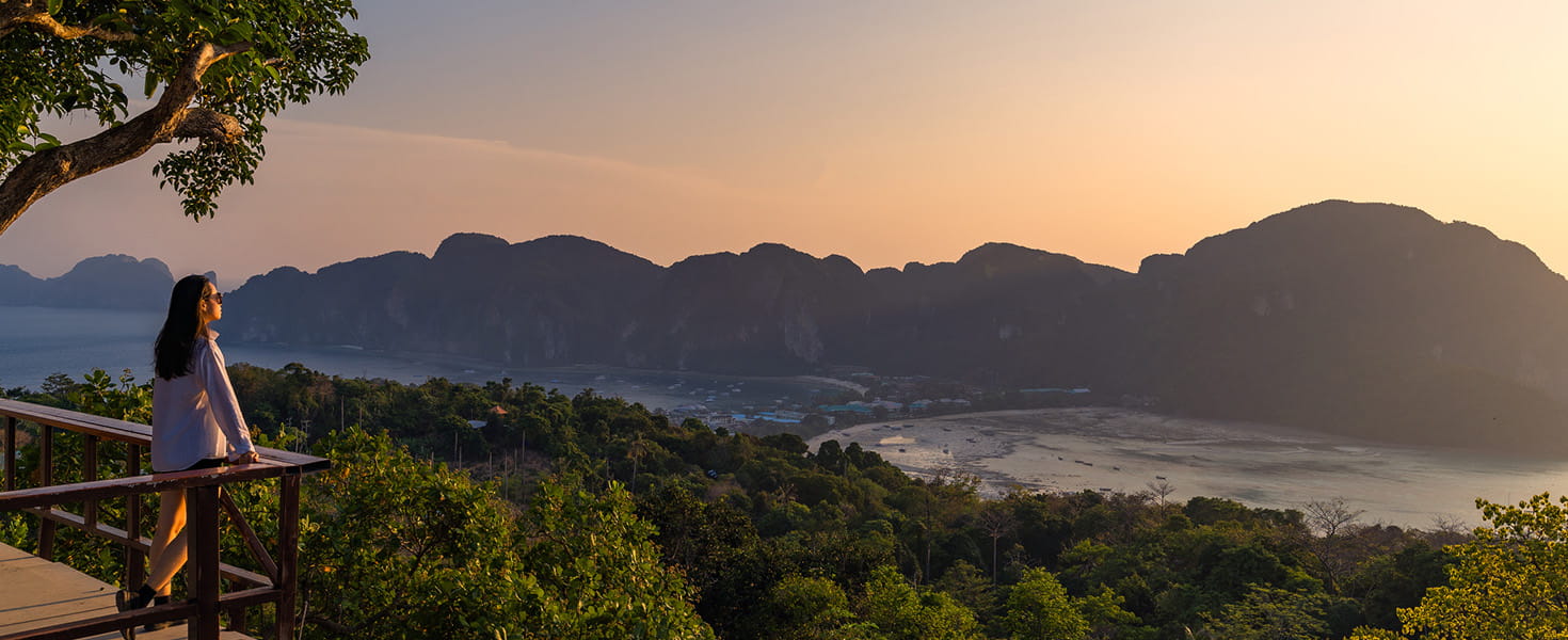 A woman standing at Phi Phi Viewpoint, overlooking the mountains, sea and the sunset. Phi Phi Island, Krabi Province, Thailand.