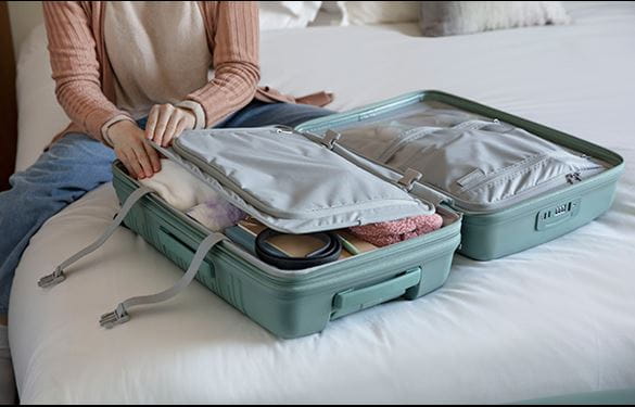 Woman packing a teal suitcase on bed