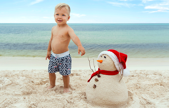 Little boy on beach with snowman made out of sand