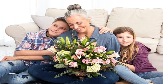 A Mother holding a big bouquet of flowers with son and daughter hugging her from each side