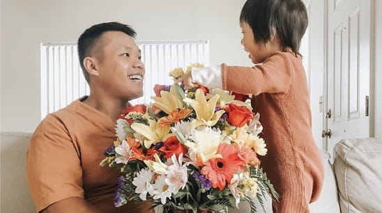 Father and baby smiling at each other while holding a bouquet of flowers