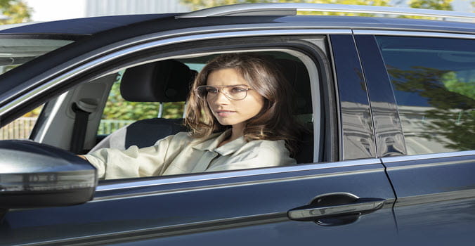 Woman driving a car with the window down wearing wire framed eyeglasses