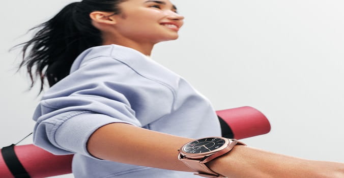 Woman carrying a rolled up yoga mat is wearing active wear and showing an up close view of her Samsung smart watch