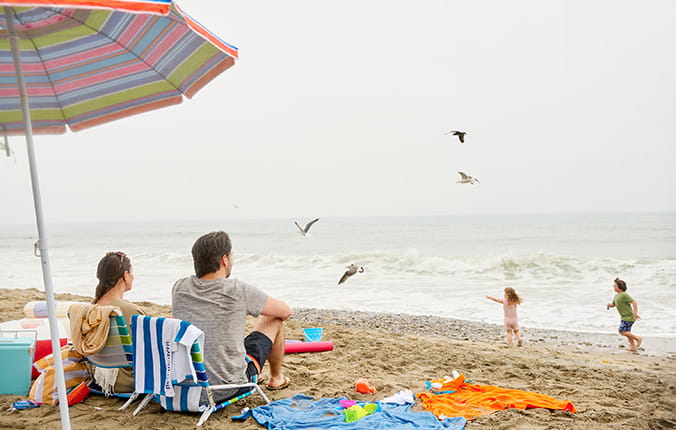 A family enjoying a day at the beach, sitting together on the sand, with the ocean waves in the background.