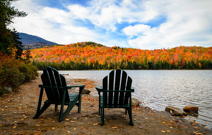 Two Adirondack chairs face scenic mountains, water and fall foliage