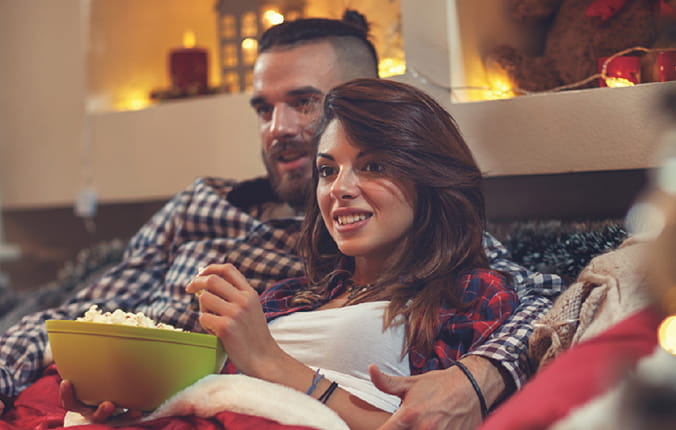 Couple on couch enjoying popcorn and watching a movie with holiday decor in background