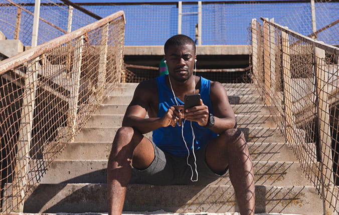 Athlete sits on stairs listening to content on his phone