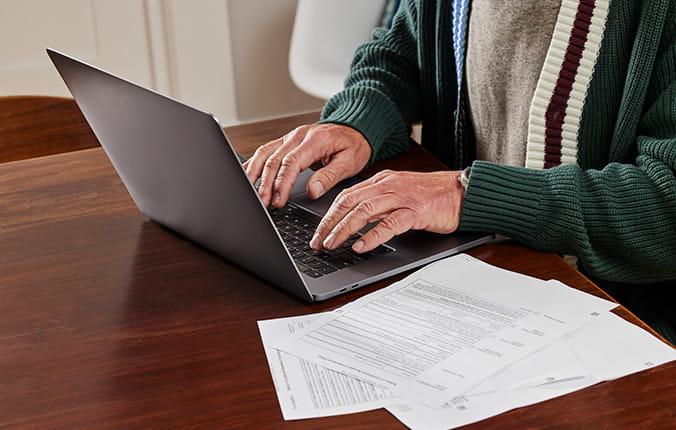 Person preparing taxes at home on their laptop, with documents on desk