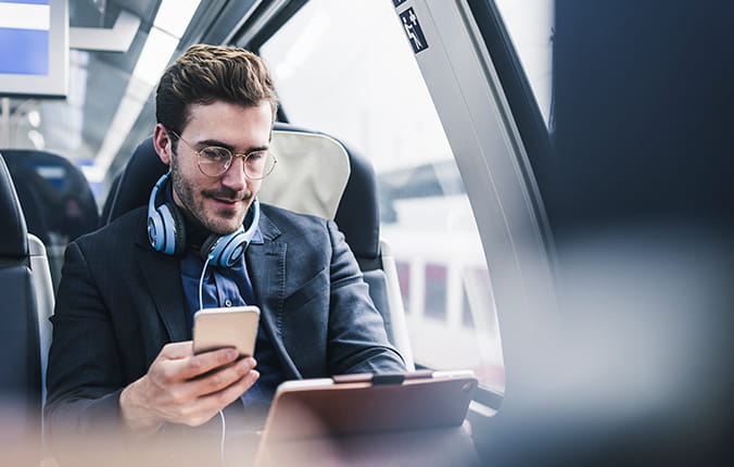 A man in a suit and headphones sitting on a train, focused on his phone screen