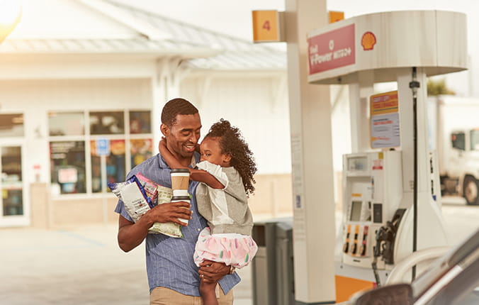 A man holding his child at a Shell gas station, along with convenience store purchases.