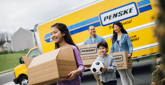 family of four carrying moving boxes from their Penske moving truck 